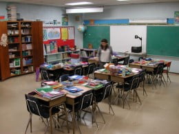Imagem de uma sala de aula com as carteiras escolares juntas e livros.
