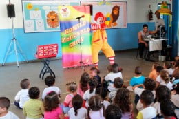 Crianças vendo um show do Ronald Mc Donalds em uma escola.