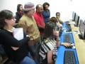 Foto mostra várias pessoas reunidas na frente de computadores