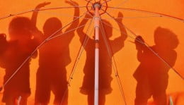 Foto mostra sombra de crianças sendo refletidas em guarda-chuva laranja. Educação integral.