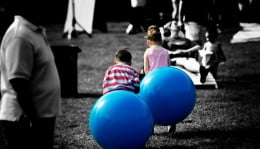 Duas crianças sentadas em bolas de ar azul, brincando no meio da cidade.