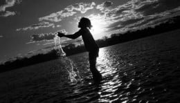 Criança brincando em um rio, no fundo o brilho do sol.