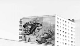 Foto de prédio com o desenho de uma mãe e duas crianças. Todos têm galhos saindo das cabeças, como se fossem árvores