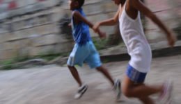 Duas crianças brincam de corrida em uma rua.