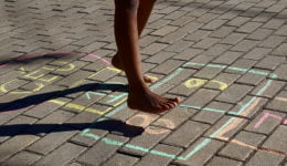 Foto mostra os pés de uma criança brincando de amarelinha