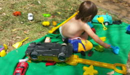 Criança de costas agachada, brincando em um tapete verde.