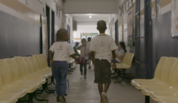Foto de uma cena do 2º episódio da série "Corações e Mentes" mostra duas crianças de costas andando em corredor de escola