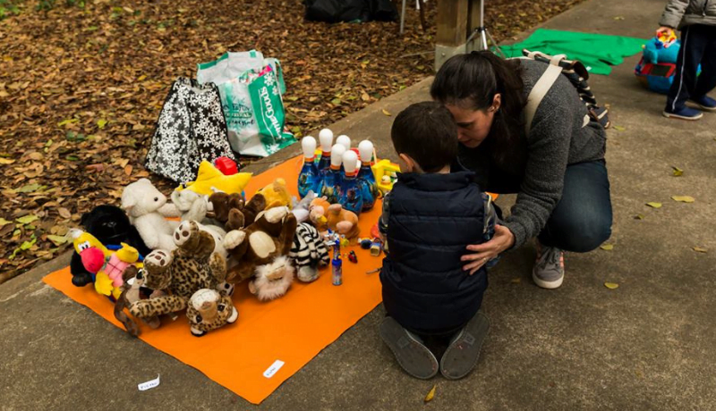 Foto da Feira de Trocas de Brinquedos mostra mãe e criança olhando para um tapete laranja com vários brinquedos