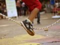 Foto de criança pulando corda. No centro da imagem aparece seus pés saltando e ao fundo está a corda.