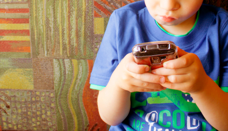Foto criança mexendo no celular, representando a necessidade de proteção das crianças no ambiente digital