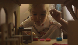 Cena de um dos filmes mostra uma criança brincando com uma casinha de bonecas