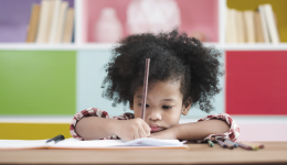 Criança escreve em um caderno apoiado sobre uma mesa. Ensino domiciliar representa retrocesso na educação.