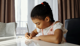 Foto mostra criança sozinha escrevendo em mesa em casa, representando o ensino domiciliar