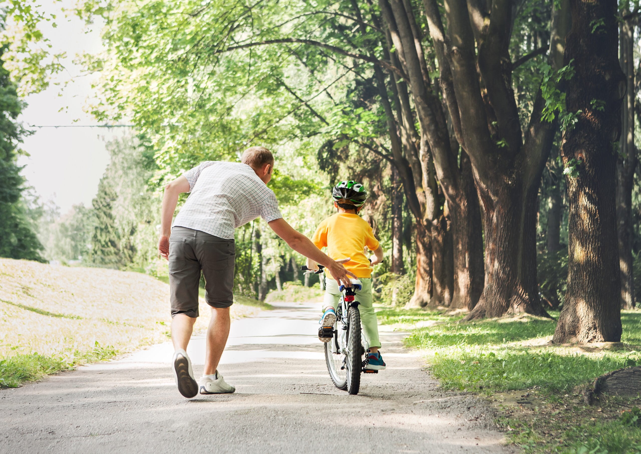 Foto mostra criança andando de bicicleta com o pai