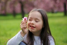 Foto mostra criança com síndrome de down segurando uma flor. somos plurais.