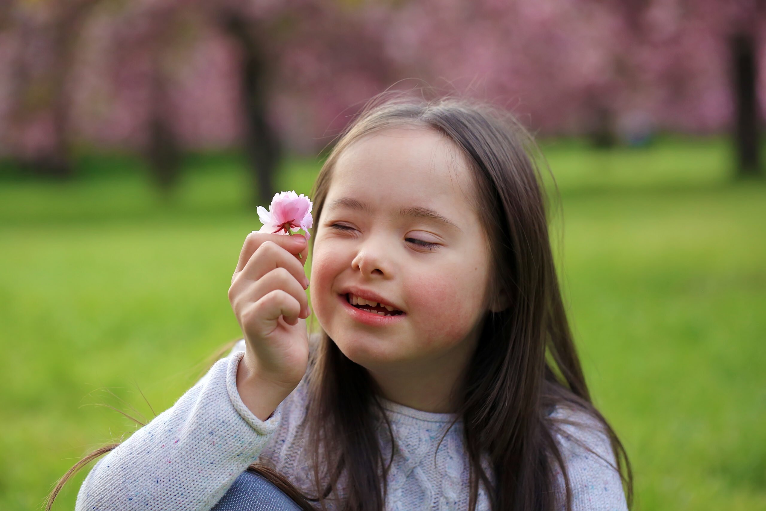 Foto mostra criança com síndrome de down segurando uma flor