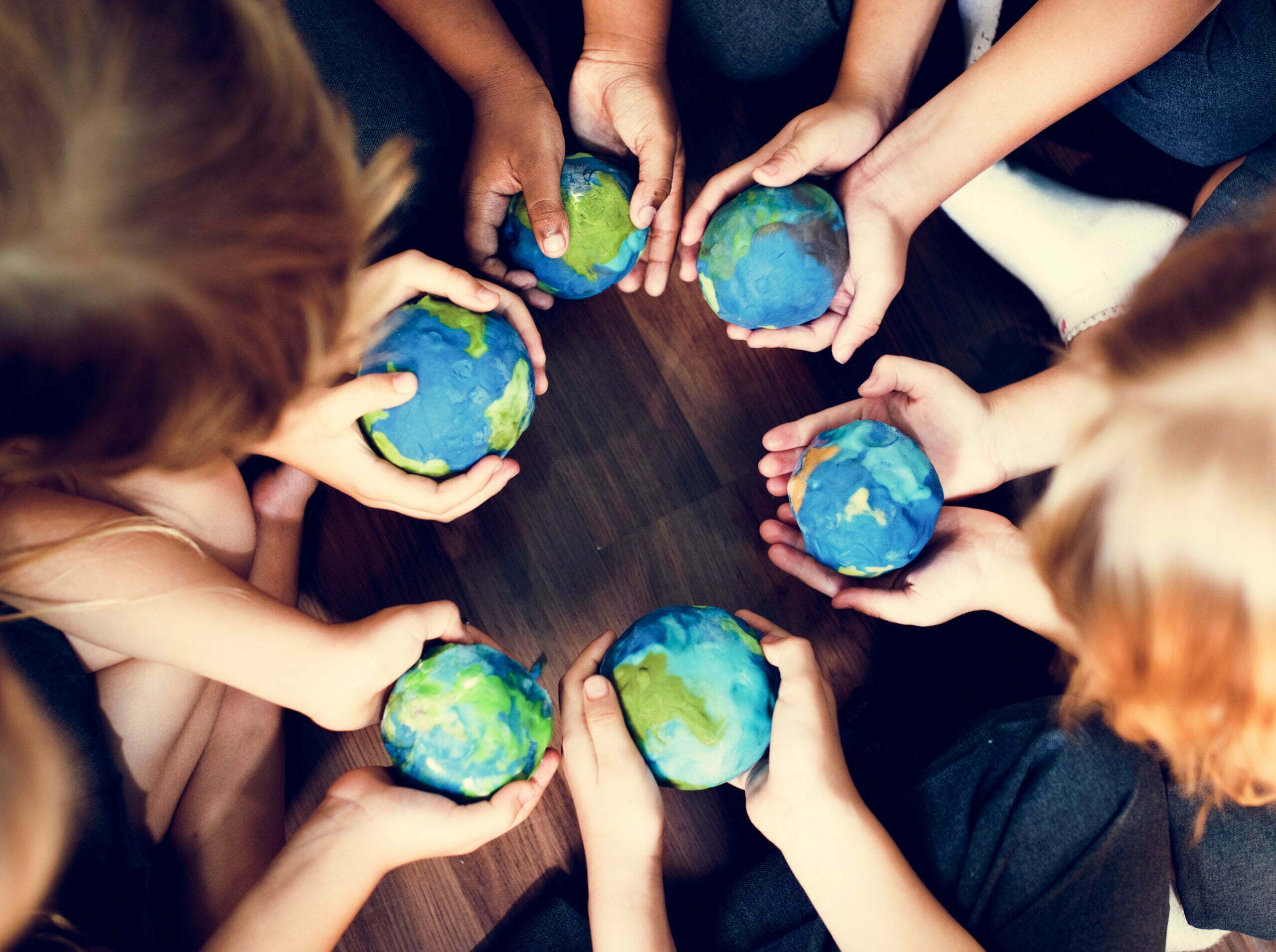 Foto mostra crianças segurando o planeta terra (feito de massinha) nas mãos