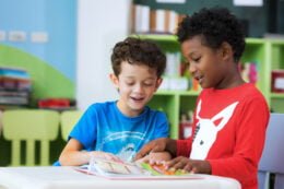 Foto mostra duas crianças, uma preta e outra branca, lendo um livro na escola. educação antirracista