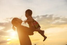 Discurso Ana Lucia Villela. Na foto, mulher ergue para o alto uma criança, ao fundo por do sol.