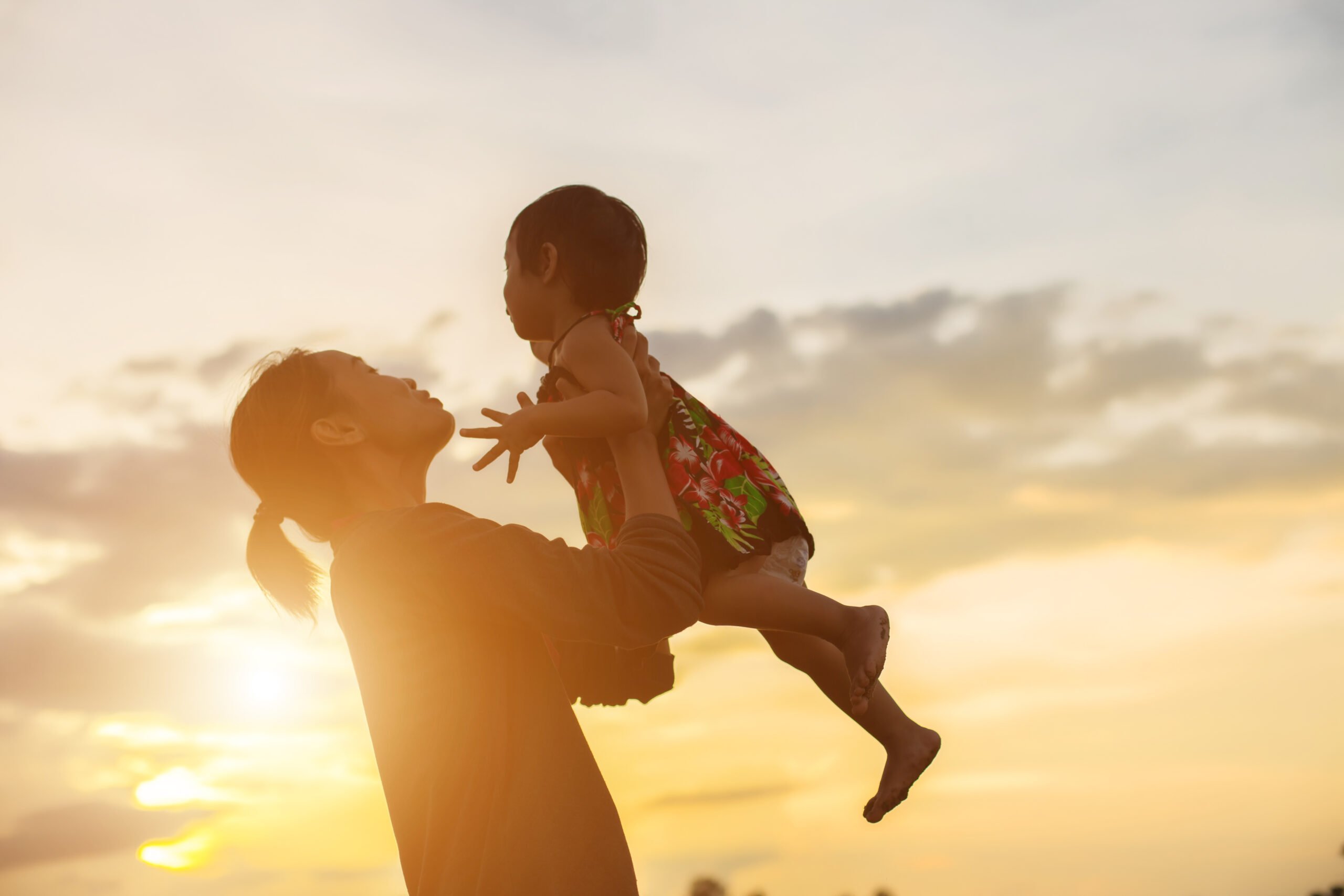 mulher ergue para o alto uma criança, ao fundo por do sol