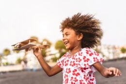 Foto de uma menina negra correndo com um aviãozinho de madeira em uma das mãos, em referência ao lançamento do material de apoio sobre educação antirracista.