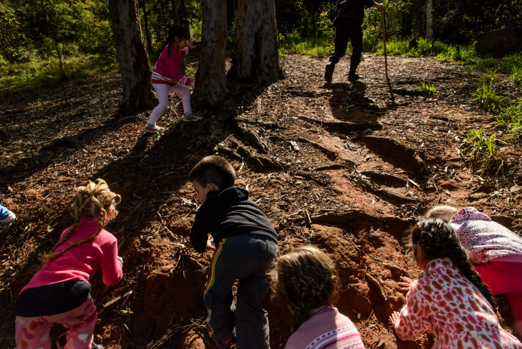 Na imagem, crianças escalam e brincam no chão de terra de um parque.
