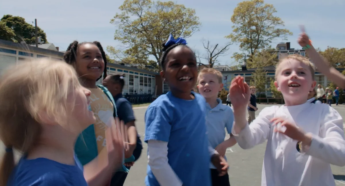 Cena do filme "Um lugar para todo mundo". Na imagem, crianças brancas e negras sorriem em um pátio escolar.