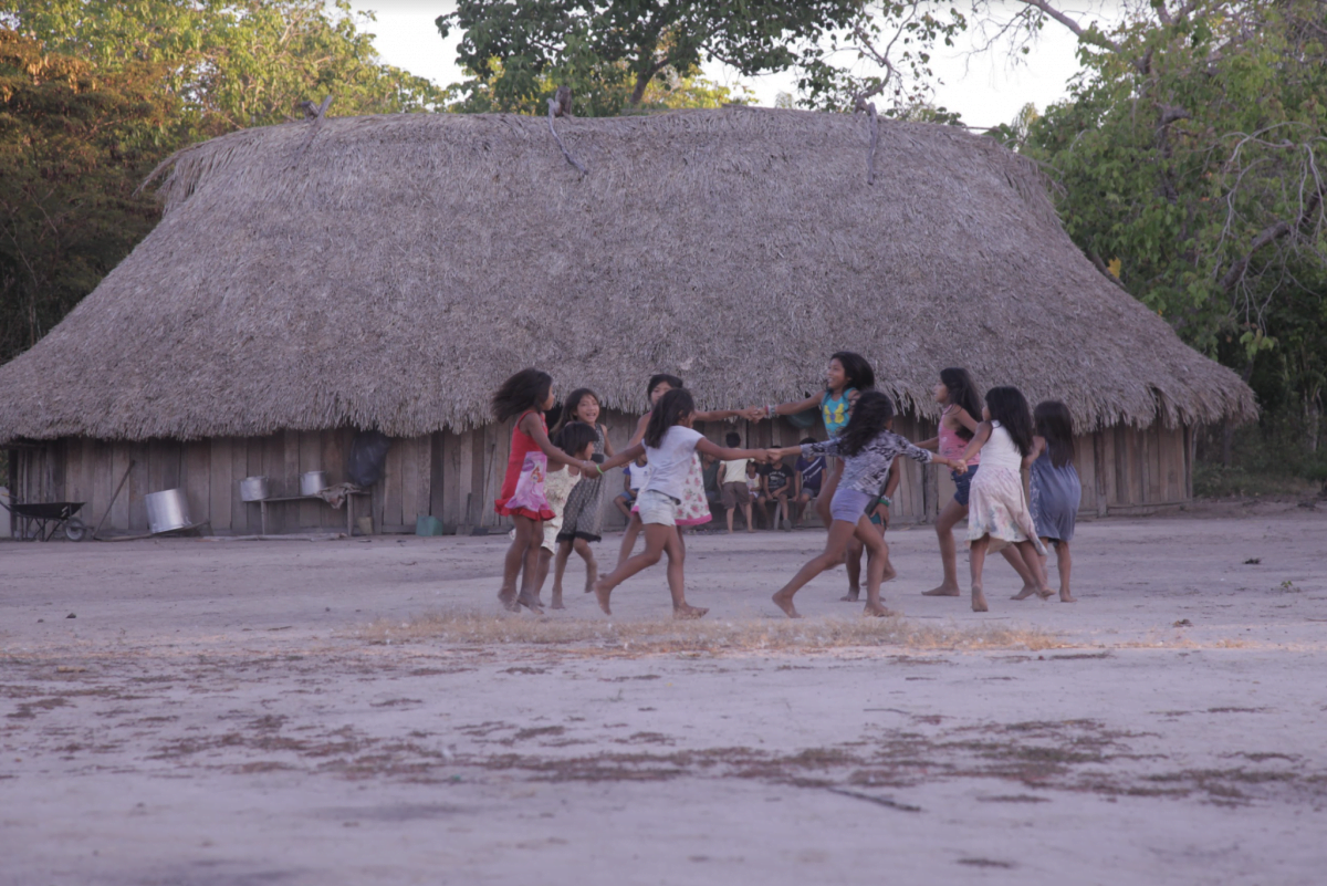 Na imagem, crianças indígenas brincam de roda em uma aldeia
