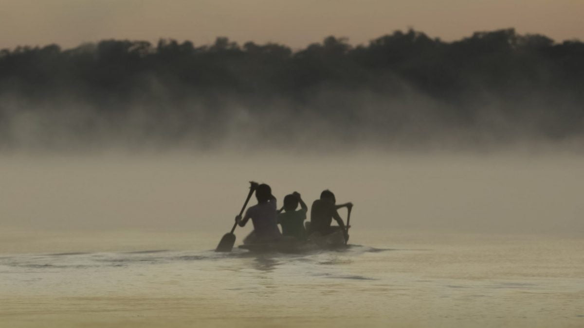 Cena do filme Waapa. Na imagem, crianças indígenas remam em um rio na floresta amazônica.