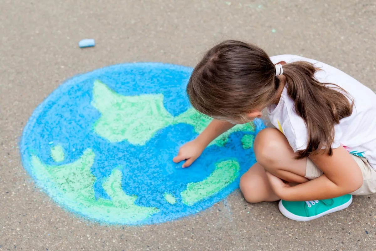Judicialização, infâncias e natureza: foto de uma criança desenhando o Planeta Terra com giz, no chão