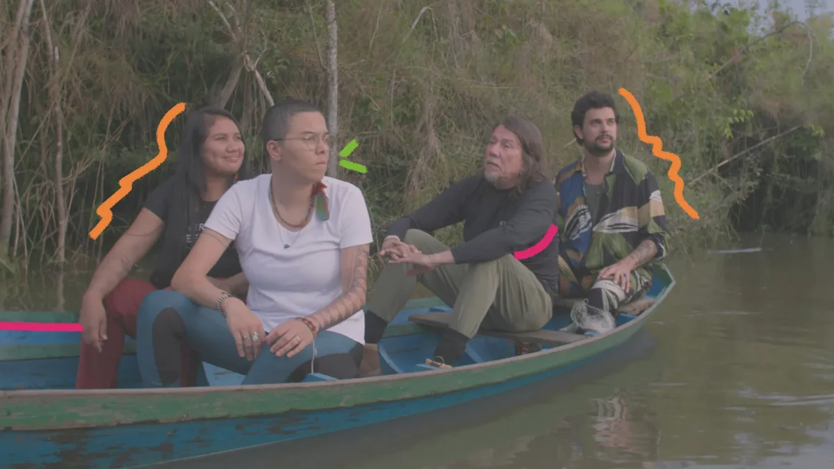 Na imagem, cena da série O Som do Rio. Quatro adultos, entre eles a cantora Maria Gadú e o cantor Lenine, estão em um barco no meio da floresta. Eles conversam e observam a paisagem.