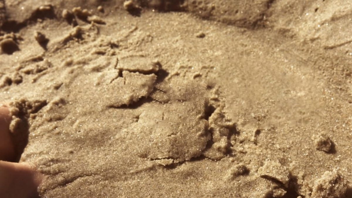 Gestos do Chão: na imagem, os pés de uma pessoa estão afundados na areia.