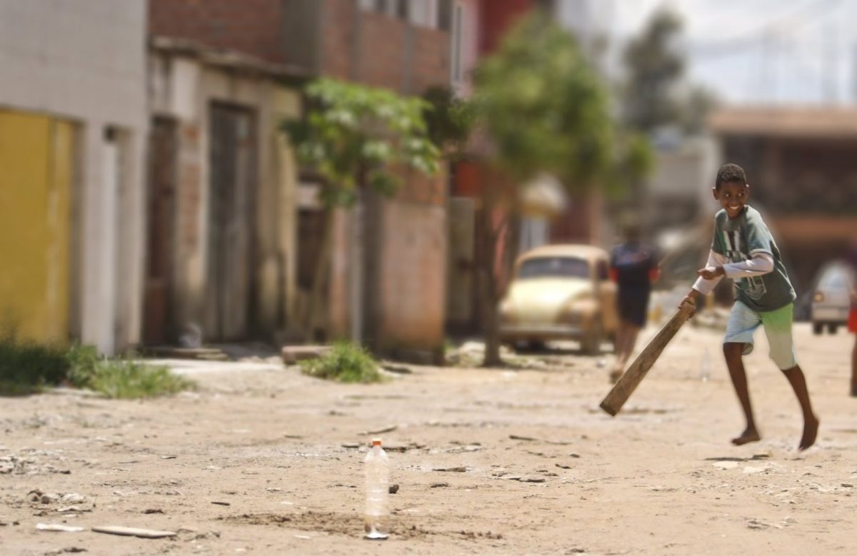 Cena do filme Território do Brincar. Na imagem, uma criança negra brinca e sorri em uma rua com chão de terra.