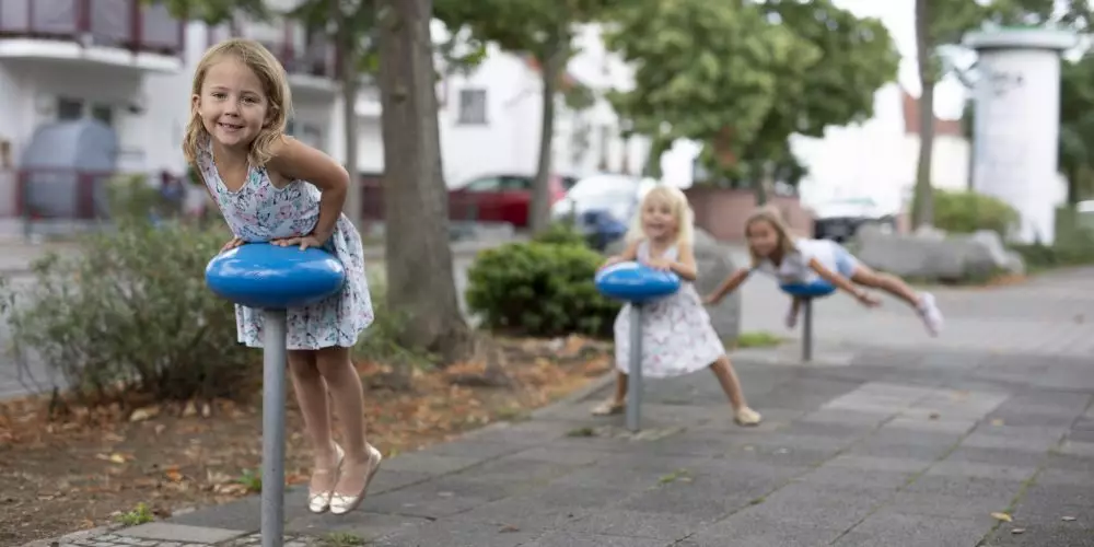 Cidades para brincar e sentar: na imagem, três crianças brancas brincam em bancos de uma praça.