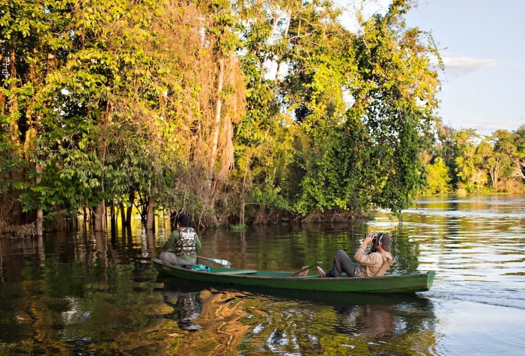 Alana XPrize Rainforest: imagem de dois adultos fazendo registros fotográficos um barco na floresta amazônica.