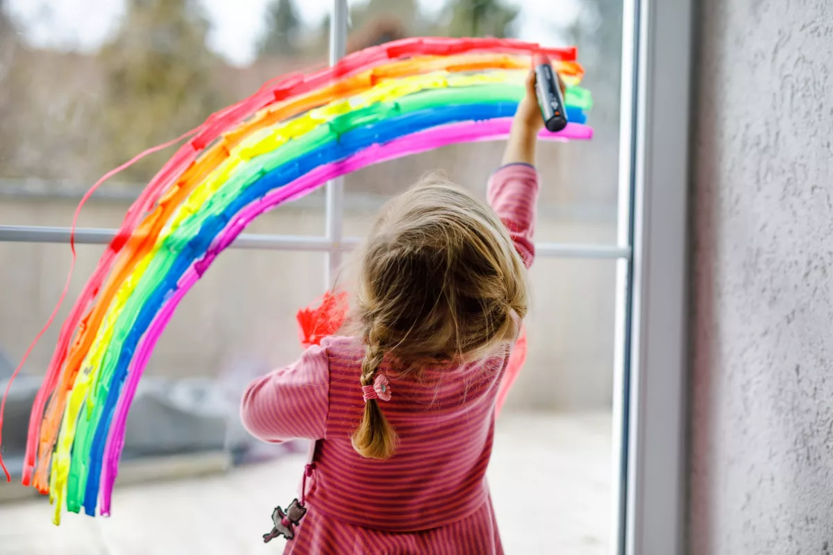 Elevate Children Funders Group: na foto, menina desenha um arco-íris em uma grande janela de vidro