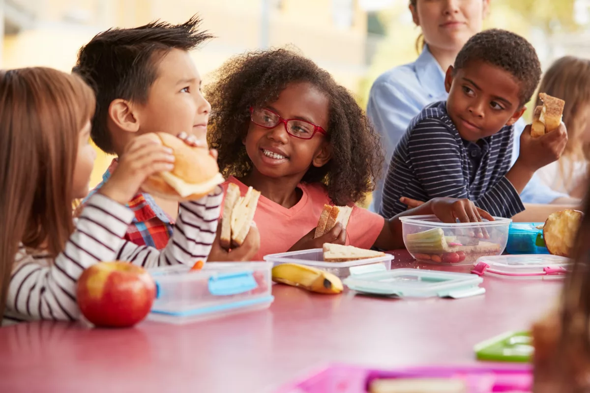 PNAE: na foto, crianças estão sentadas em uma mesa fazendo uma refeição no ambiente escolar