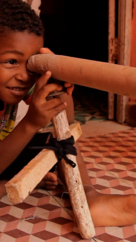 Foto de uma criança olhando por um cilindro de papelão, como se fosse uma luneta.