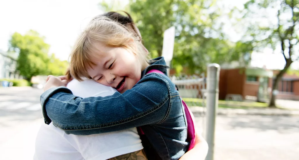 Criança branca com síndrome de Down abraça um adulto.