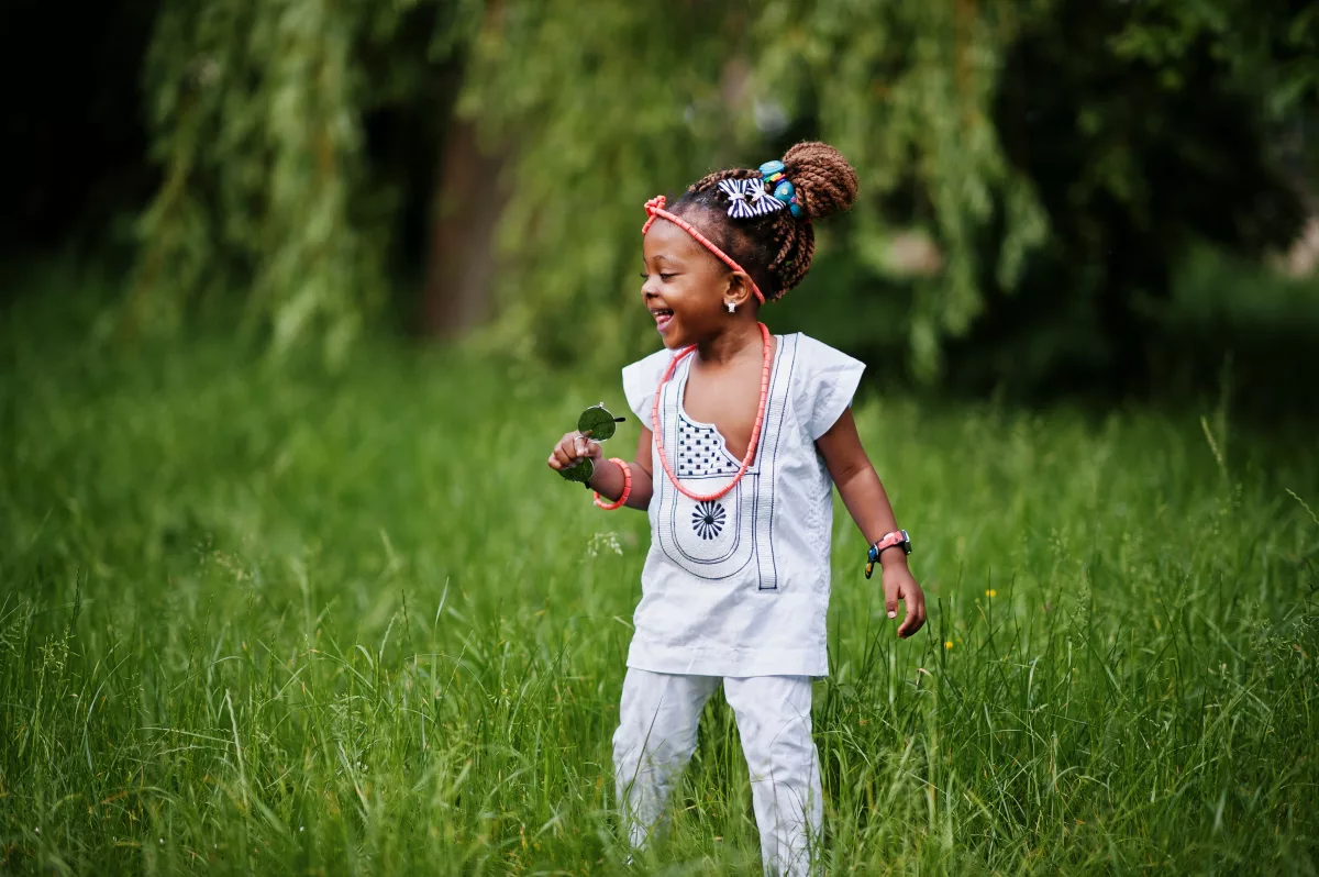 Recomendações do Alana à ONU: na foto, uma menina negra sorri em um espaço gramado, com muitas árvores ao fundo.
