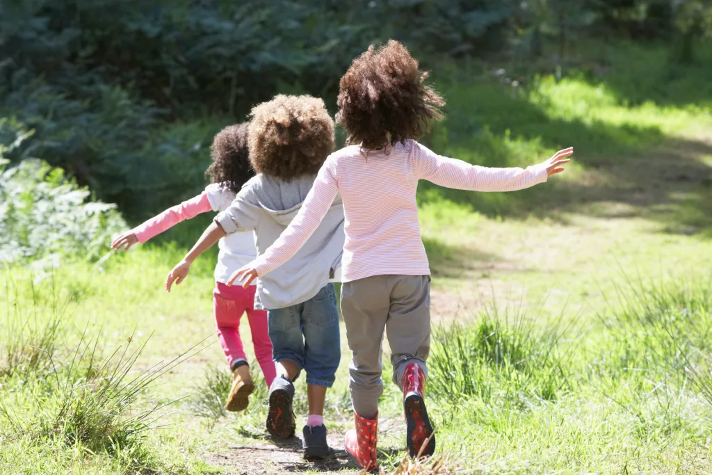 COP: três crianças negras estão, em fila, caminhando em um bosque arborizado.