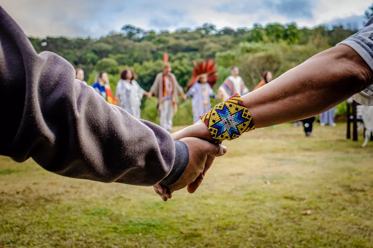 Direitos de crianças indígenas na ONU e Marco Temporal: na foto, pessoas de diferentes etnias formam um círculo e dão as mãos em um campo arborizado