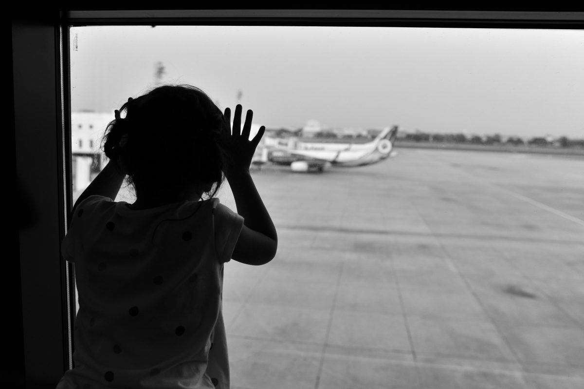 Convenção de Haia: criança olha para um avião através de uma grande janela do aeroporto