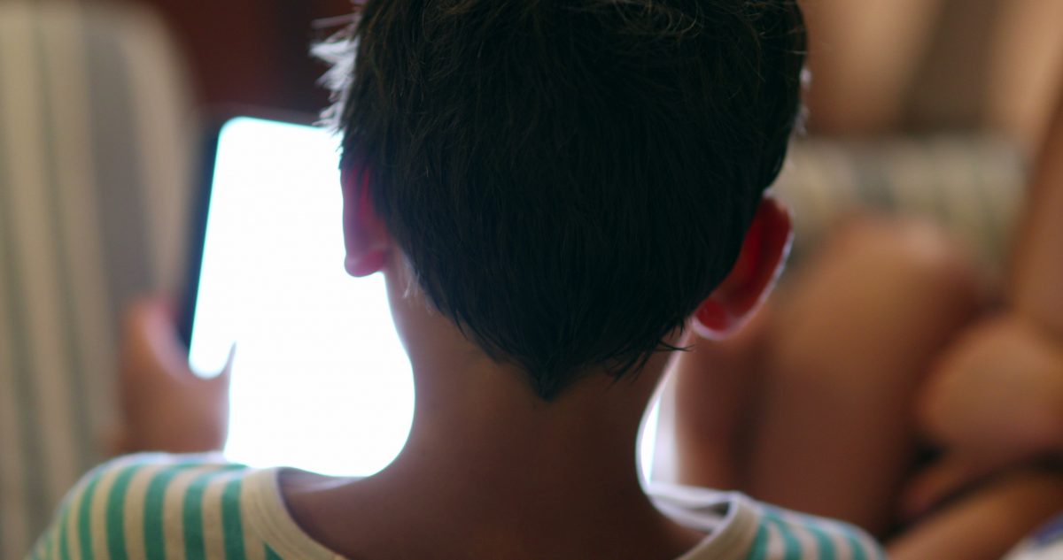 Contribuições sobre combate ao abuso e à exploração sexual infantil no ambiente digital: na foto, uma criança branca aparece de costas, mexendo em um tablet