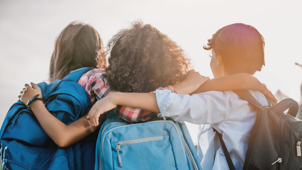 Educação inclusiva e bilíngue: na foto, três crianças de costas caminham abraçadas